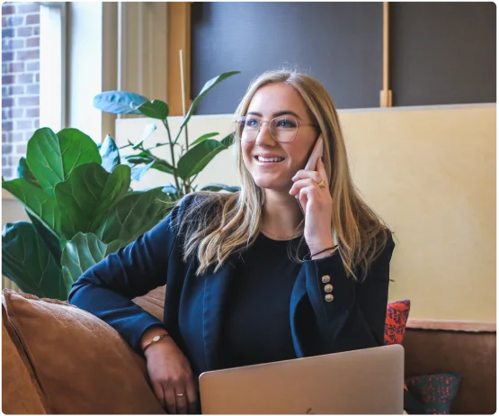 Empresária sorridente falando ao telefone enquanto trabalha no notebook em escritório moderno