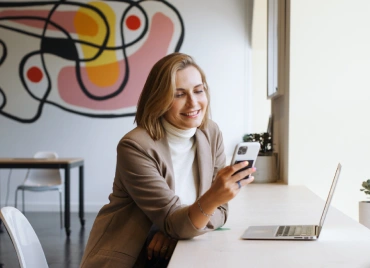 Empreendedora sorridente usando o celular em seu espaço de trabalho